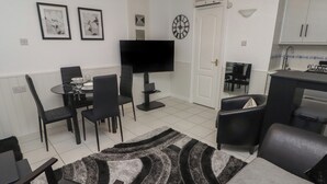 A modern living room with a flat-screen TV, dining area with chairs, a sofa, and a kitchen area with cabinets. - Flat 7 (Tenby)
