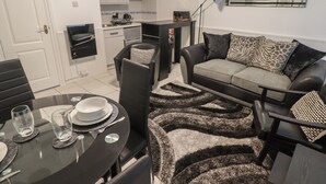 A modern living room with a sofa, a dining table set for two, and a kitchen area in the background. - Flat 7 (Tenby)