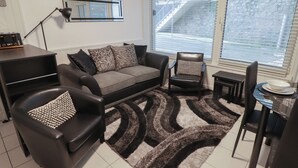 A modern living room with a sofa, armchairs, a coffee table, and a dining area. - Flat 7 (Tenby)