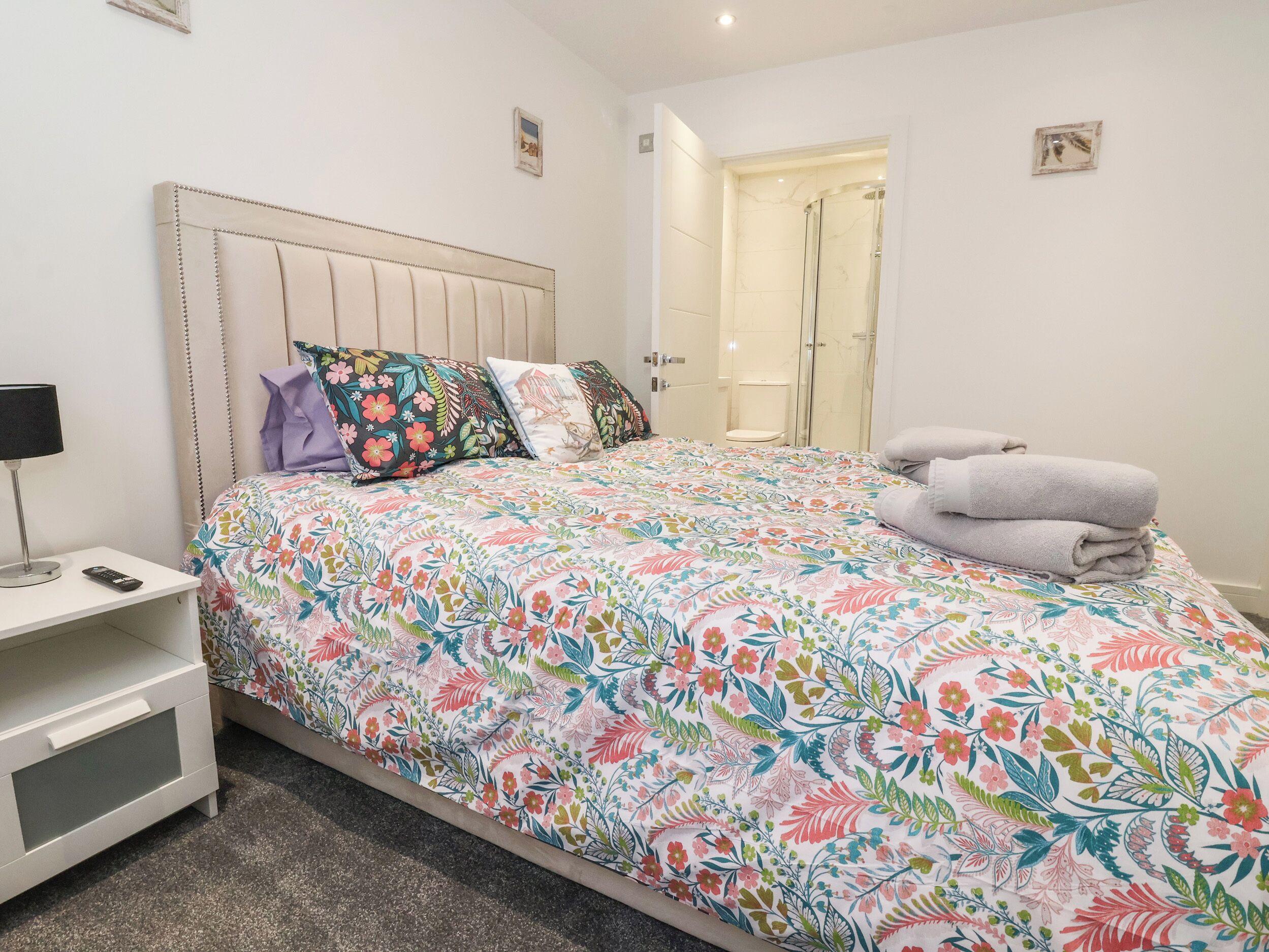A neatly made bed with floral bedding, a bedside table with a lamp, and a bathroom visible through an open door.