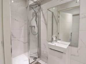 Un baño moderno con ducha de vidrio, lavabo blanco y un espejo grande.