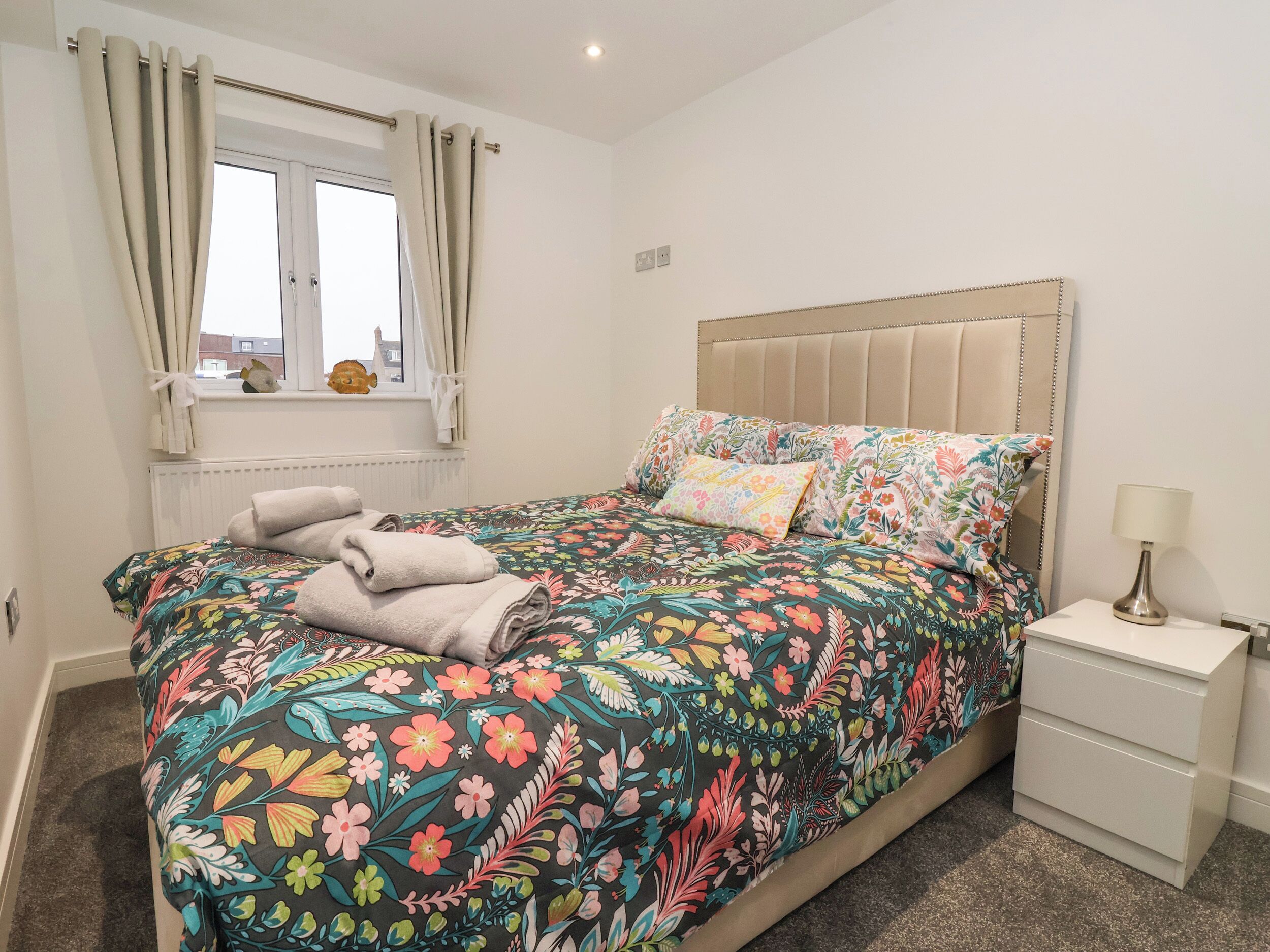 A bedroom with a bed, a window with curtains, a bedside table with a lamp, and a radiator.