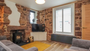 A cozy living room with stone walls, a fireplace, a television, and two grey sofas. - Woodman Cottage (Morecambe)