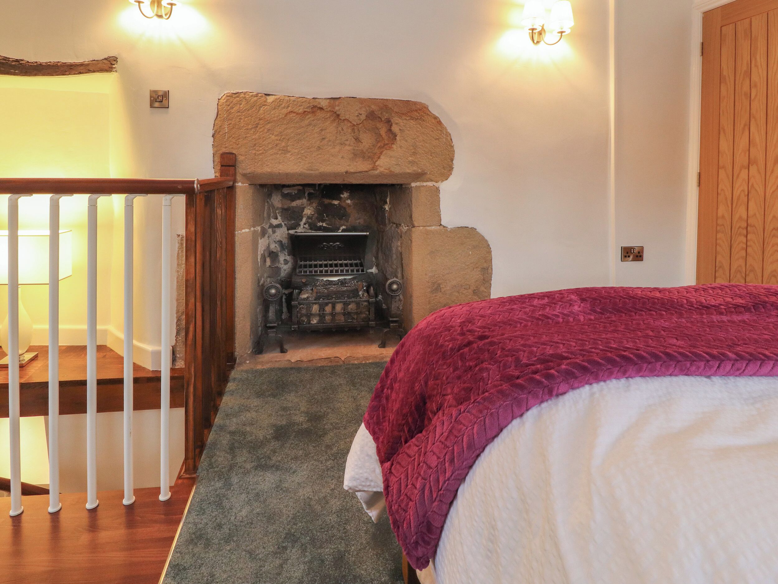 A room with a stone fireplace, a wooden staircase, and a bed with a purple blanket.