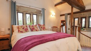 A bedroom with a large bed, a wooden headboard, a nightstand, a lamp, and a window with curtains. - Pear Tree Cottage at Hey Farm (Barnoldswick)