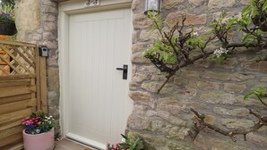 A stone wall with a white door, a wooden gate, and two flower pots with pink flowers. - Pear Tree Cottage at Hey Farm (Barnoldswick)