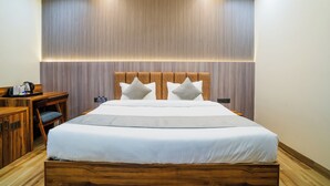 A neatly arranged hotel room with a large bed, a wooden headboard, a desk with a chair, and a wall-mounted air conditioner.