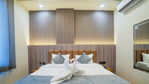 A hotel room with a large bed, a headboard with vertical slats, and a wall-mounted air conditioner.