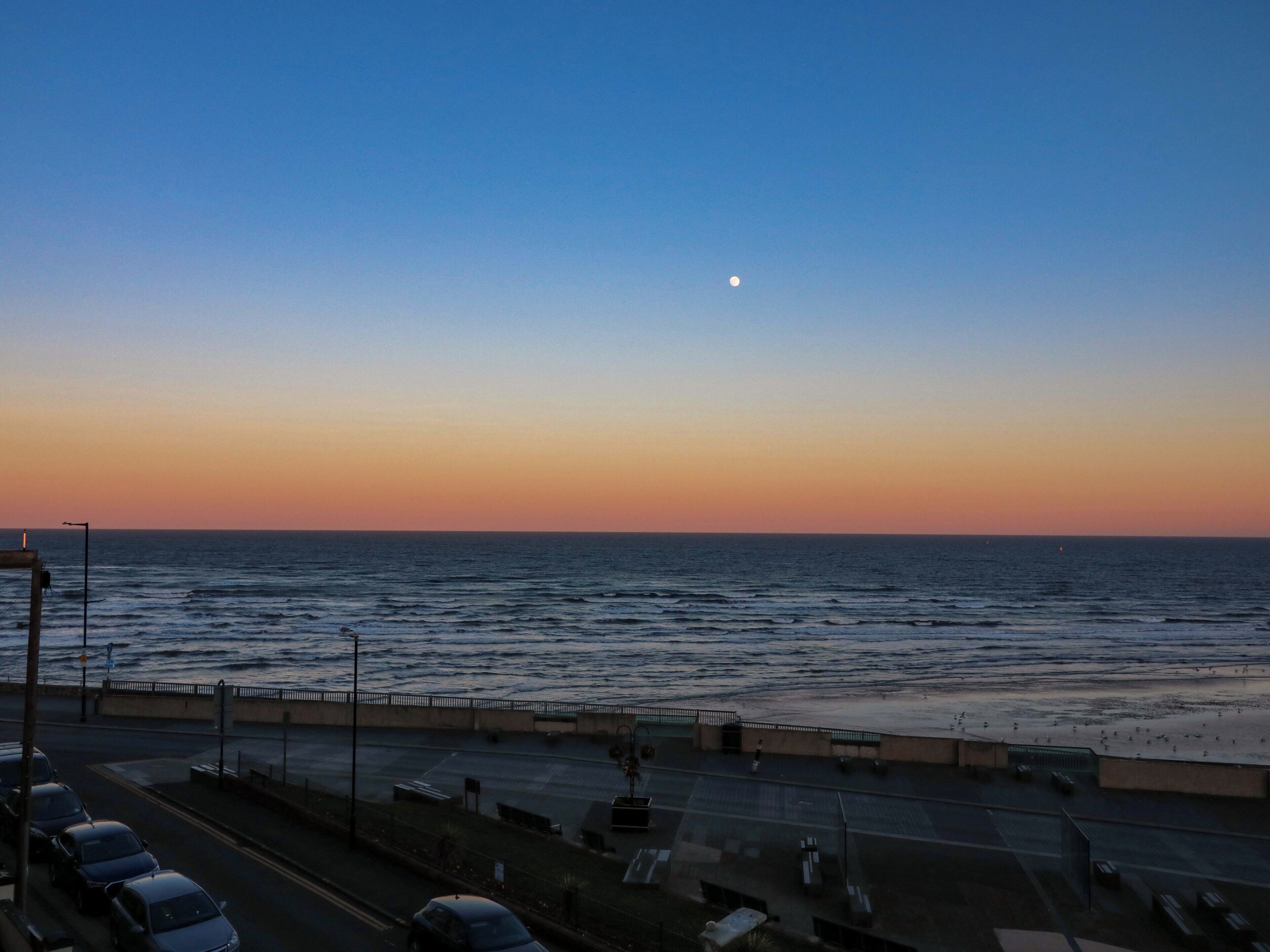 A coastal road with a view of the sea and a moon in the sky.
