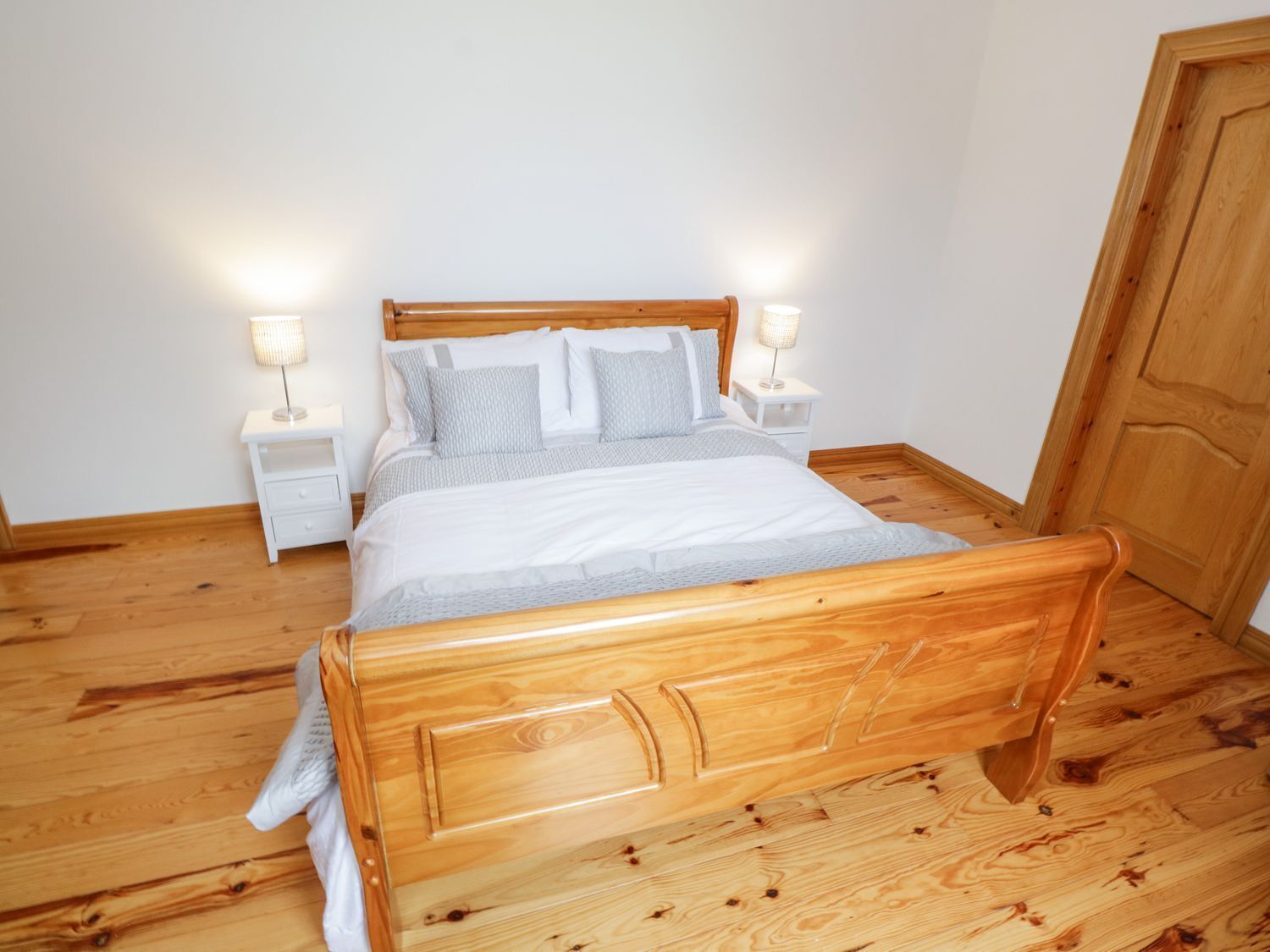 A wooden bed in a room with white walls and a wooden floor. There are two bedside tables with lamps.