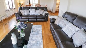 A modern living room with a black leather sofa, a glass coffee table, and a vase with flowers. - Doonalton House (Doonaltan)
