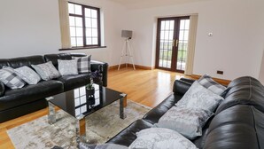 A spacious living room with a black leather sofa, a glass coffee table, and a large window providing natural light. - Doonalton House (Doonaltan)