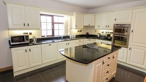 A spacious kitchen with white cabinetry, a central island, a microwave, a kettle, and a double oven. - Doonalton House (Doonaltan)