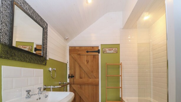 Une salle de bain avec une porte en bois, un lavabo blanc et une étagère en bois.