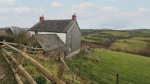 Une maison de campagne avec un toit en pente, entourée d’une clôture en bois et d’un champ herbeux.
