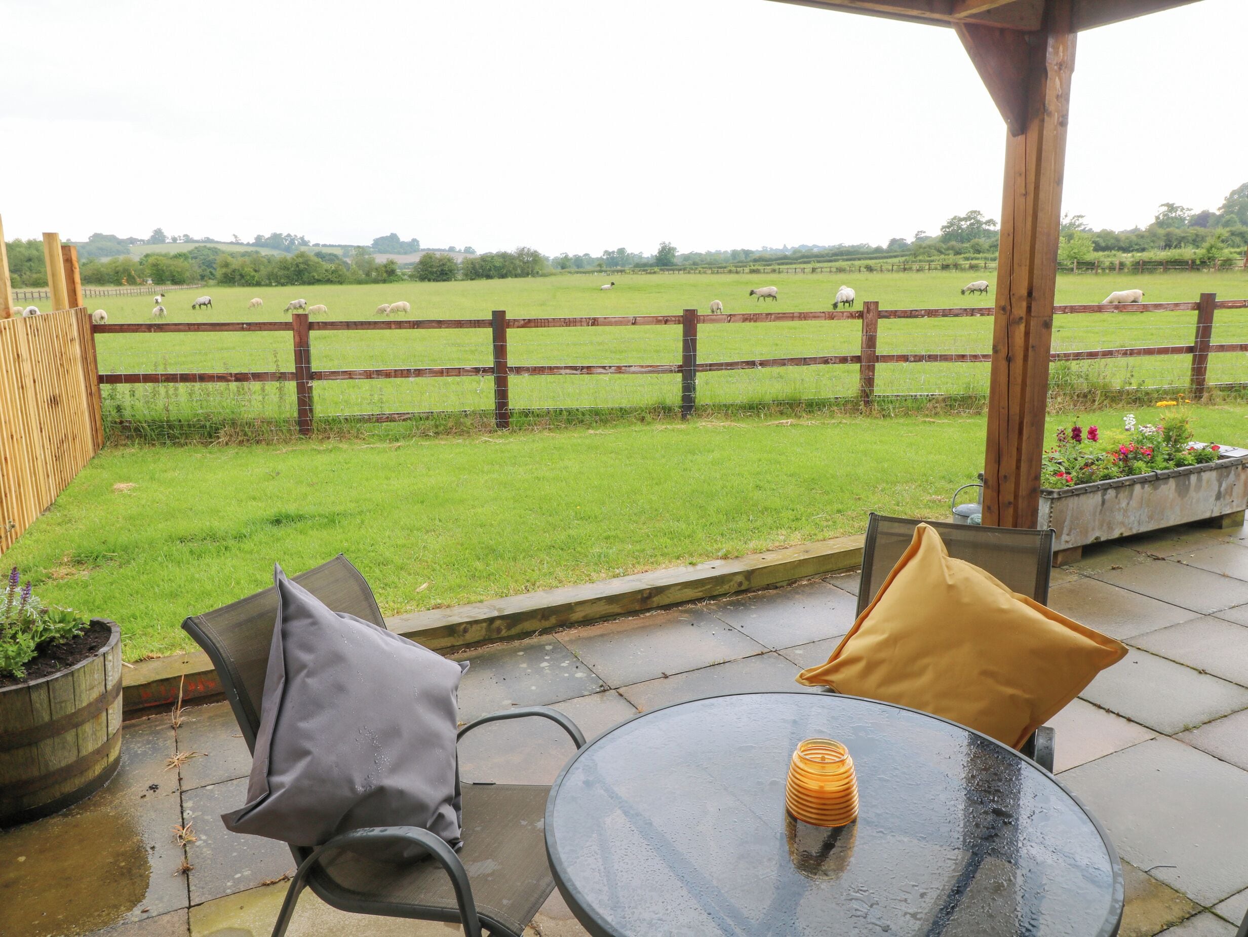 A patio with two chairs and a table, overlooking a fenced field with sheep.