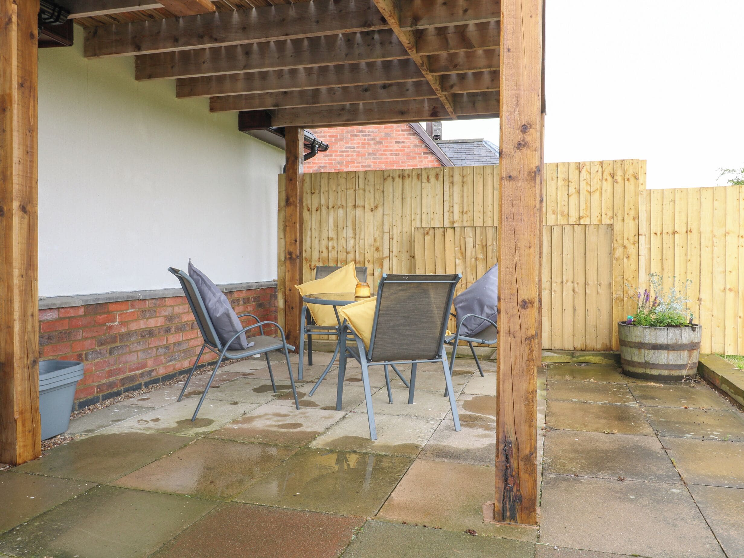 An outdoor patio with a wooden pergola, a brick wall, and a wooden fence.