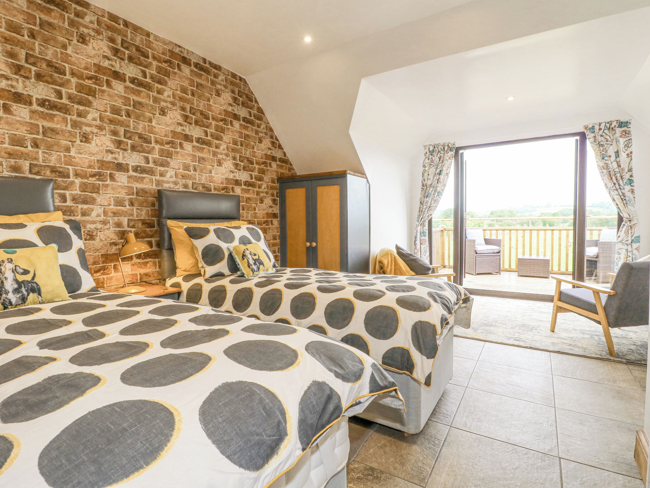 A bedroom with a brick wall, a large bed with patterned bedding, a wardrobe, and a balcony with outdoor furniture.