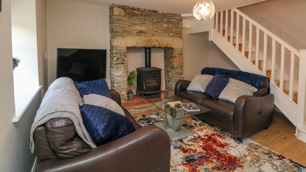 A cozy living room with two leather sofas, a stone fireplace, a glass coffee table, and a staircase. - An Teach Ban (Bunclody)