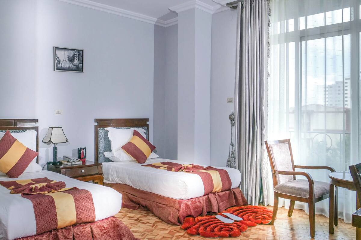 Une chambre d’hôtel avec deux lits, un bureau, une chaise et une grande fenêtre avec des rideaux.