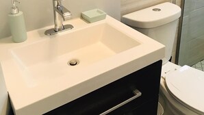 Une salle de bain moderne avec un lavabo blanc, un miroir, des toilettes et un espace douche.