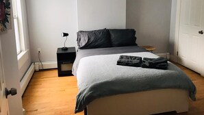 Une chambre à coucher avec un lit, une table de chevet avec une lampe, un petit tabouret en bois et une porte.