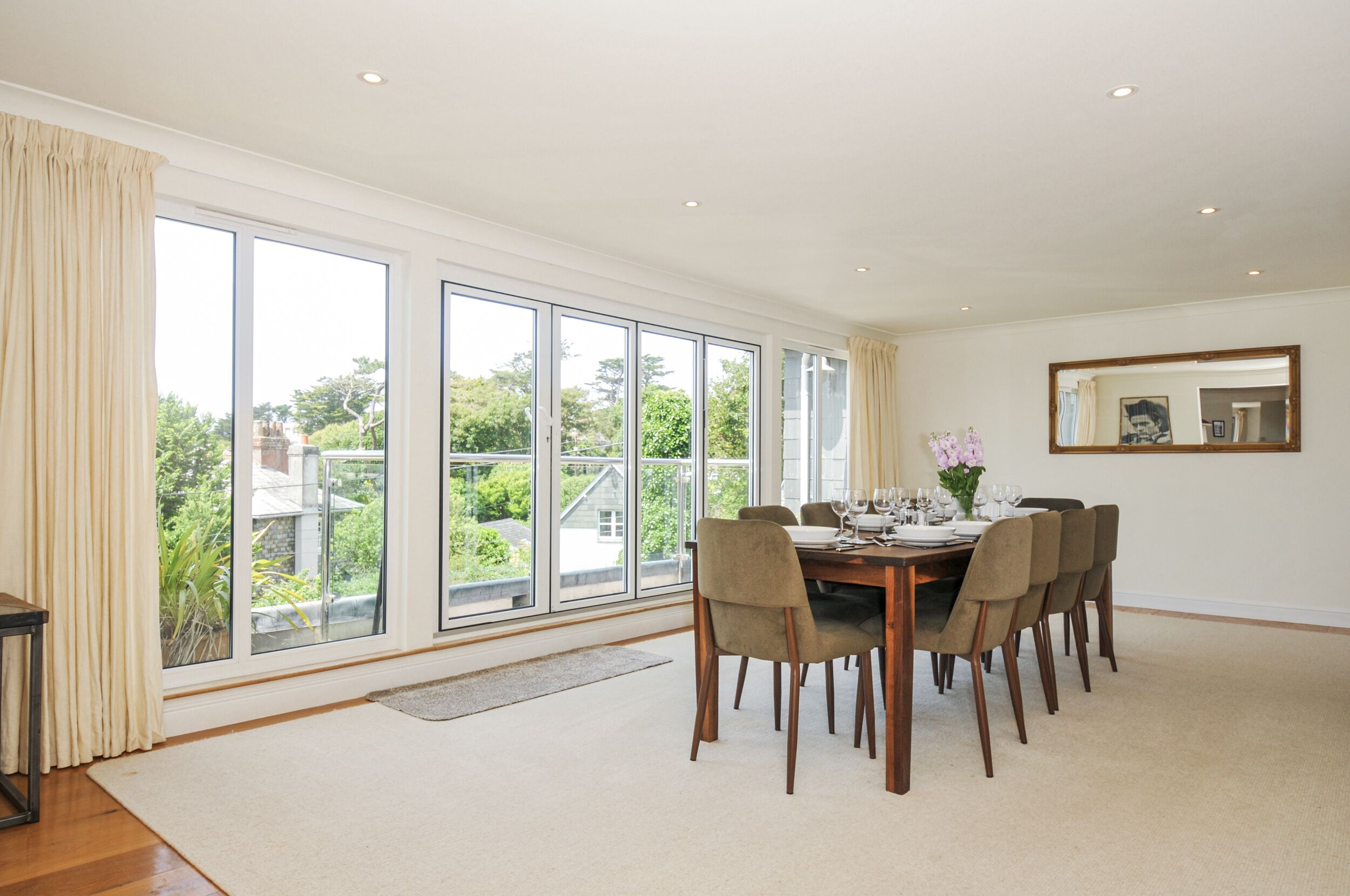 A dining room with a large window, a dining table set for six, and a mirror on the wall.