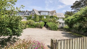A large house with a gravel driveway, surrounded by lush greenery and flowering plants. - Bodare 8 (Wadebridge)