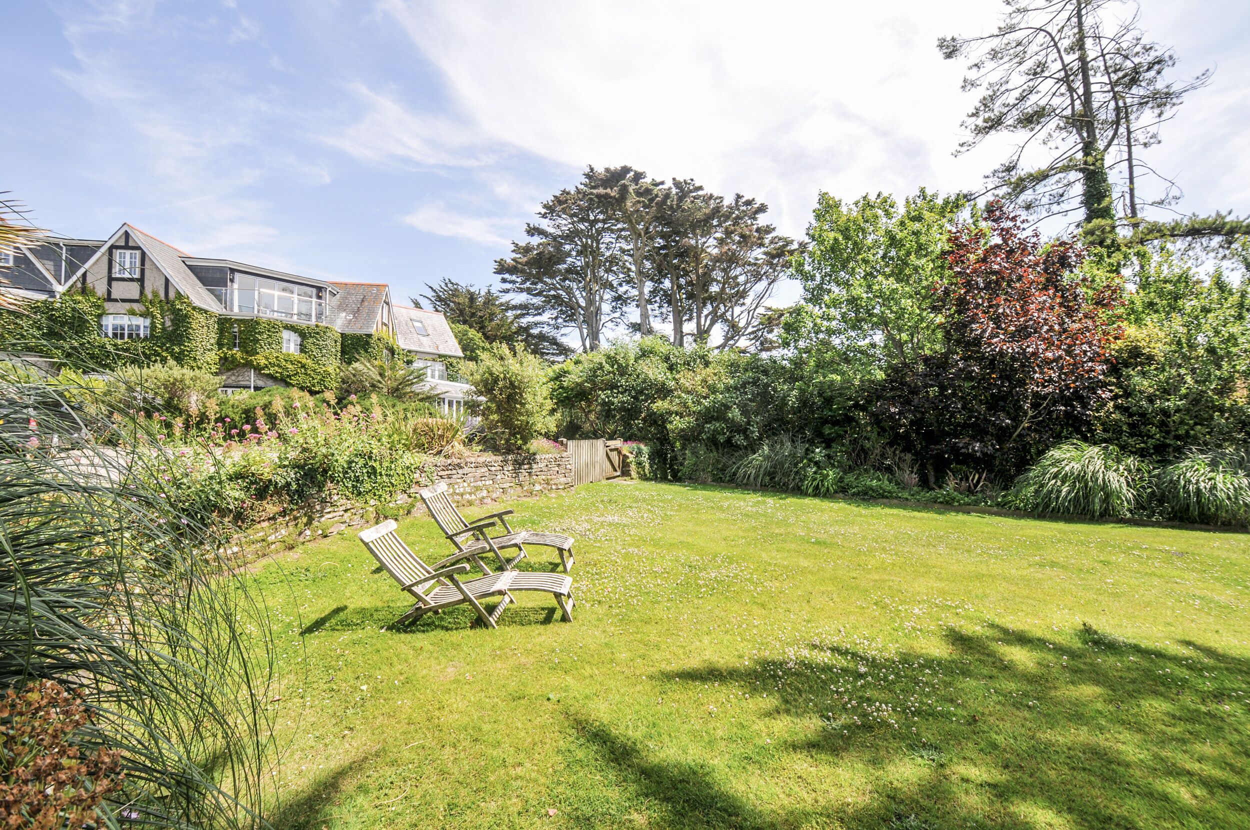 A well-maintained garden with a lawn, a wooden bench, and a stone wall.