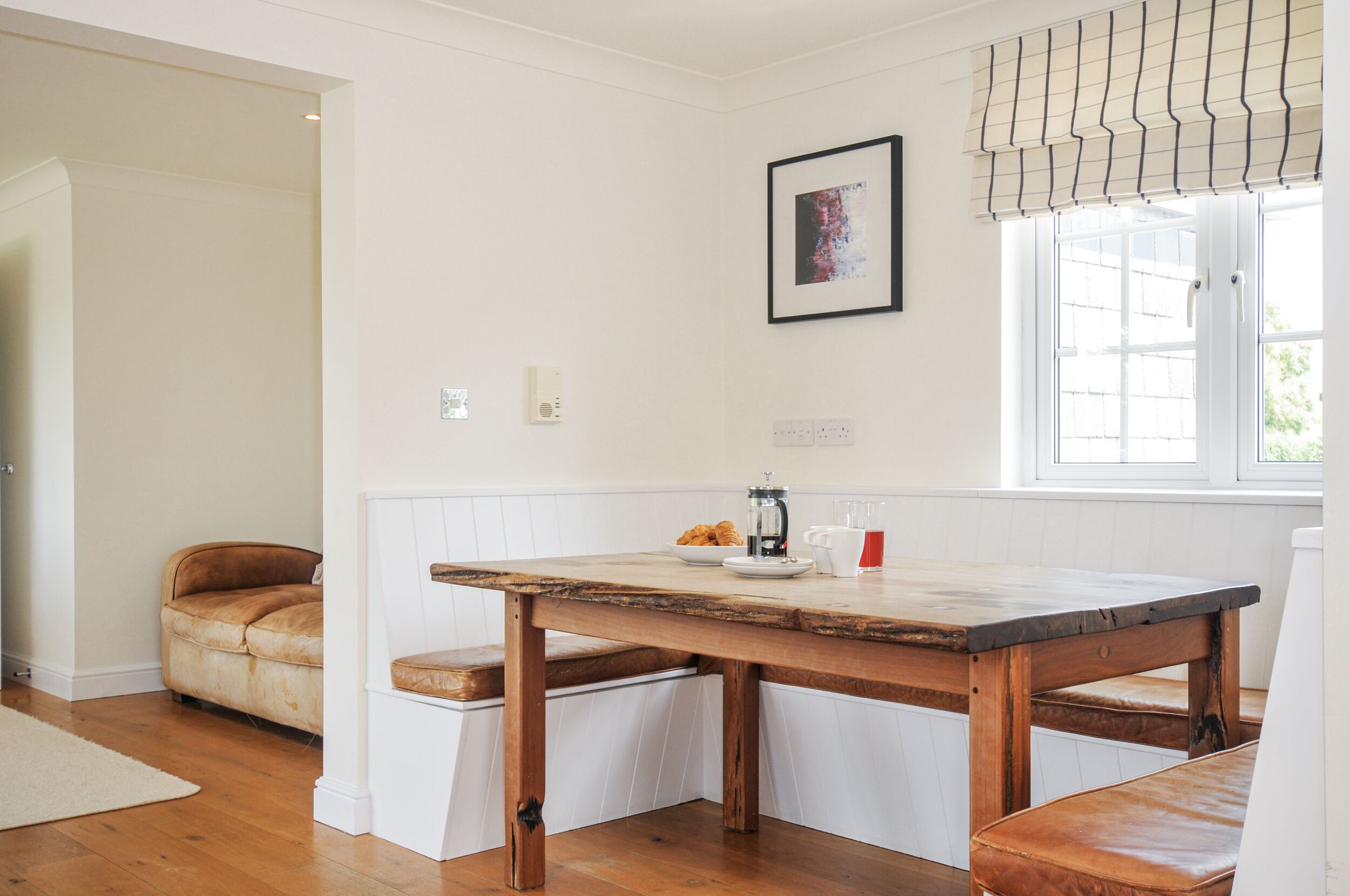 A dining area with a wooden table, bench seating, a window with blinds, and a framed picture on the wall.