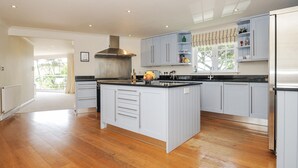 A spacious kitchen with a large central island, light blue cabinets, and a stainless steel range hood. - Bodare 8 (Wadebridge)