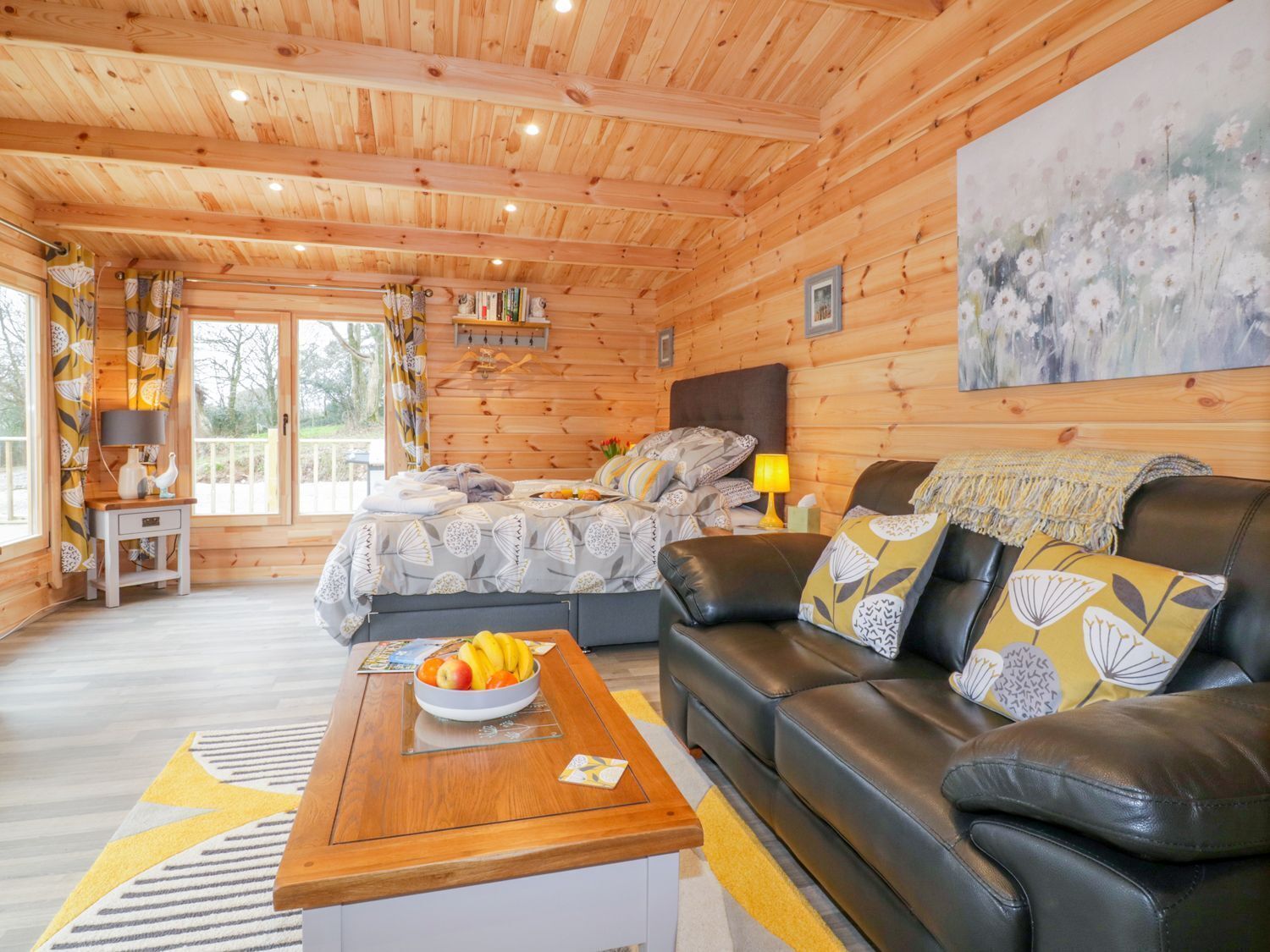 Ein gemütliches Schlafzimmer in einer Blockhütte mit einem Bett, einem Sofa, einem Esstisch mit Obst und einem Bild an der Wand.