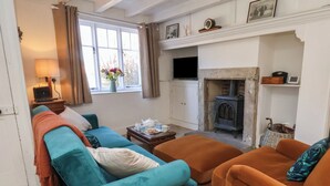 Una sala de estar con un conjunto de sofás, una chimenea, un televisor y una ventana con cortinas.