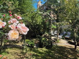 Un jardín con rosas florecientes, una pérgola de madera y un muro de piedra.