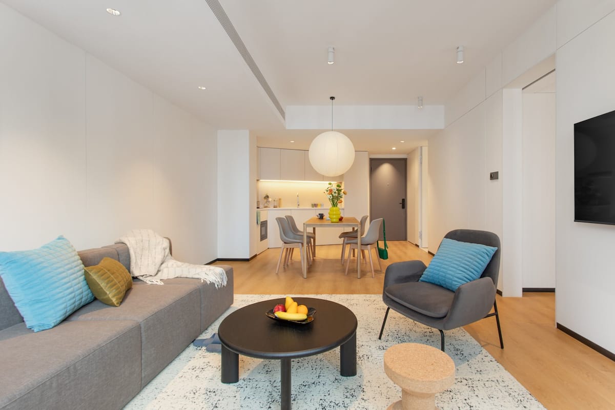 Ein modernes Wohnzimmer mit Sofa, Sesseln, Couchtisch und einem Essbereich mit Tisch und Stühlen.
