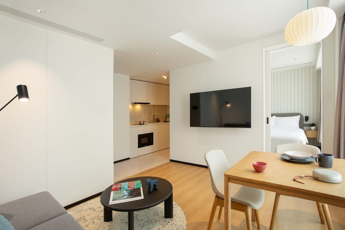 Ein modernes Hotelzimmer mit Essbereich, einem flachbildfernseher an der Wand und einer gemütlichen Sitzecke mit kleinem Tisch und Stühlen.
