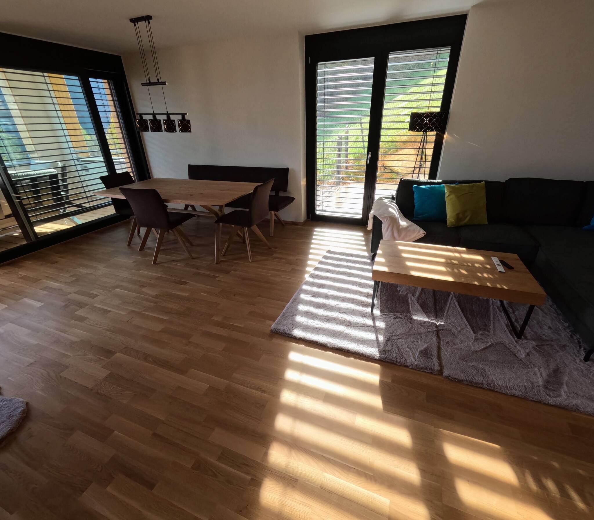 Ein modernes Wohnzimmer mit Holzboden, einem Esstisch mit Stühlen, einem Sofa und einem Couchtisch.