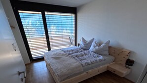 A bedroom with a bed, wooden floor, and a window with blinds. - Charming Family Apartment in Bürserberg Österreich (Buerserberg)