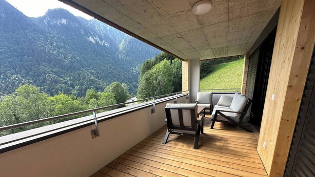 A balcony with wooden flooring, two chairs, and a table. A view of a mountainous landscape is visible through the railing. - Charming Family Apartment in Bürserberg Österreich (Buerserberg)