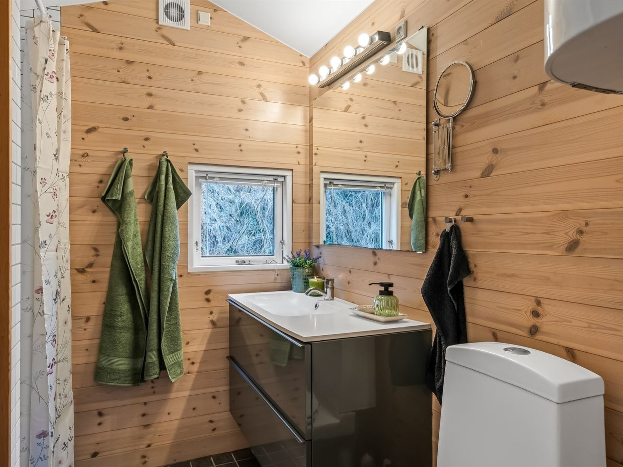 Un baño moderno con paredes de madera, un espejo grande, un lavamanos y un inodoro.
