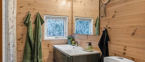 Un baño moderno con paredes de madera, un espejo grande, un lavamanos y un inodoro.
