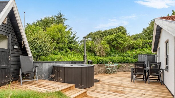 Una terraza de madera con jacuzzi, mobiliario exterior y una parrilla.