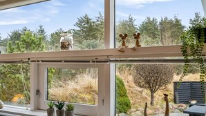 Habitación con un ventanal grande que da a un jardín. Hay plantas en macetas en el alféizar y una pequeña mesa con una silla afuera.