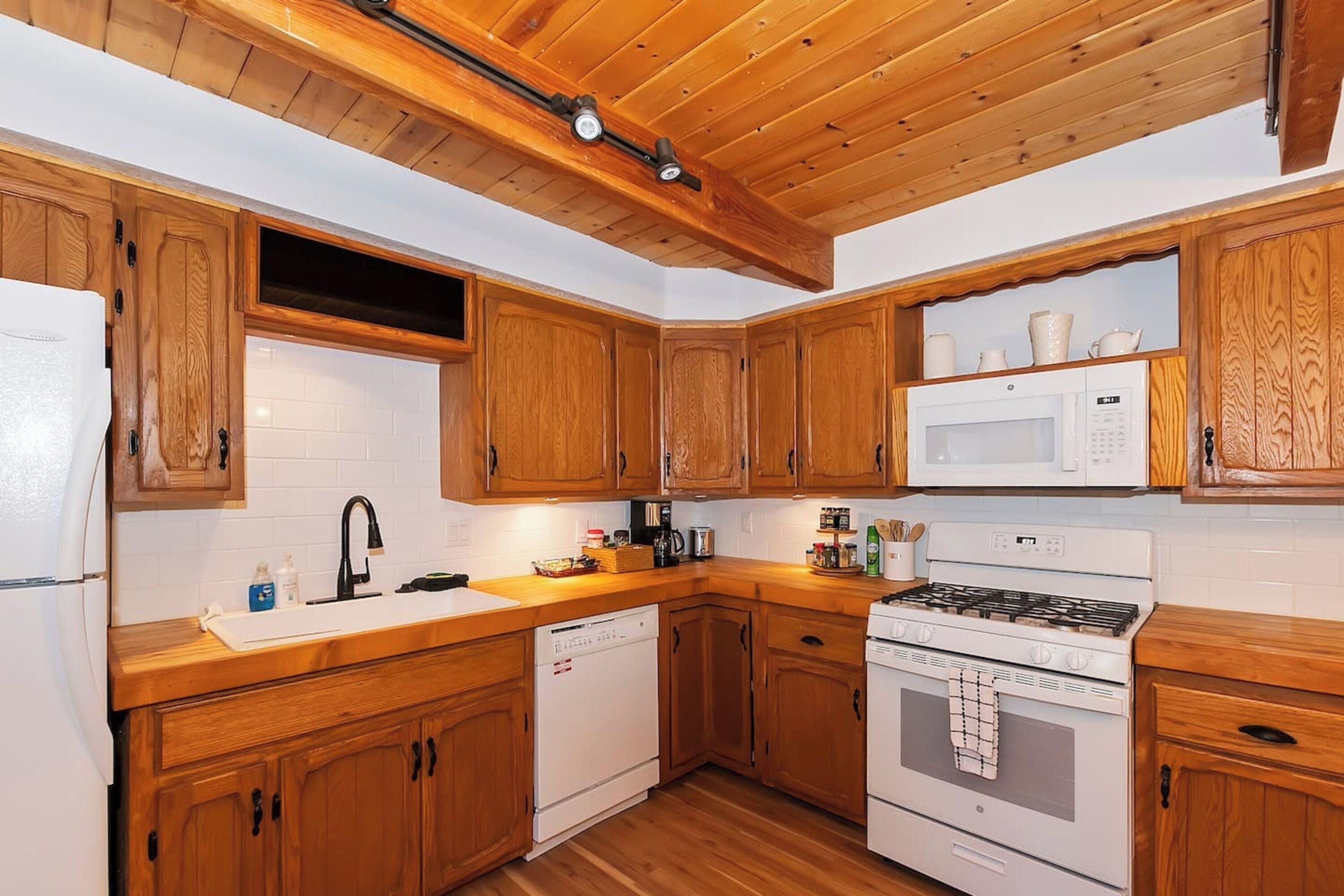 A kitchen with wooden cabinets, a white refrigerator, a microwave, a stove, and a dishwasher.