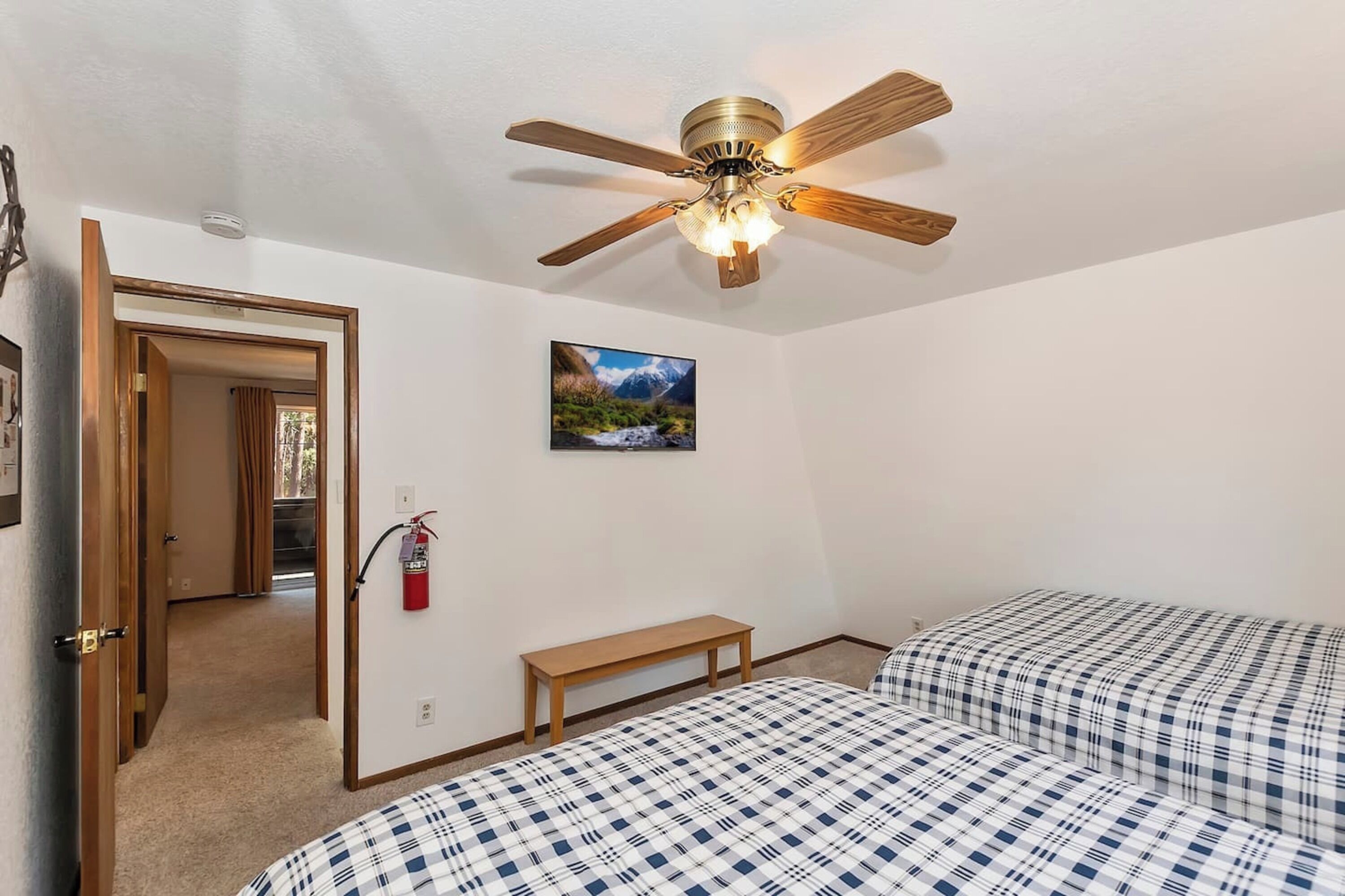 A bedroom with two beds, a ceiling fan, a fire extinguisher, and a picture on the wall.