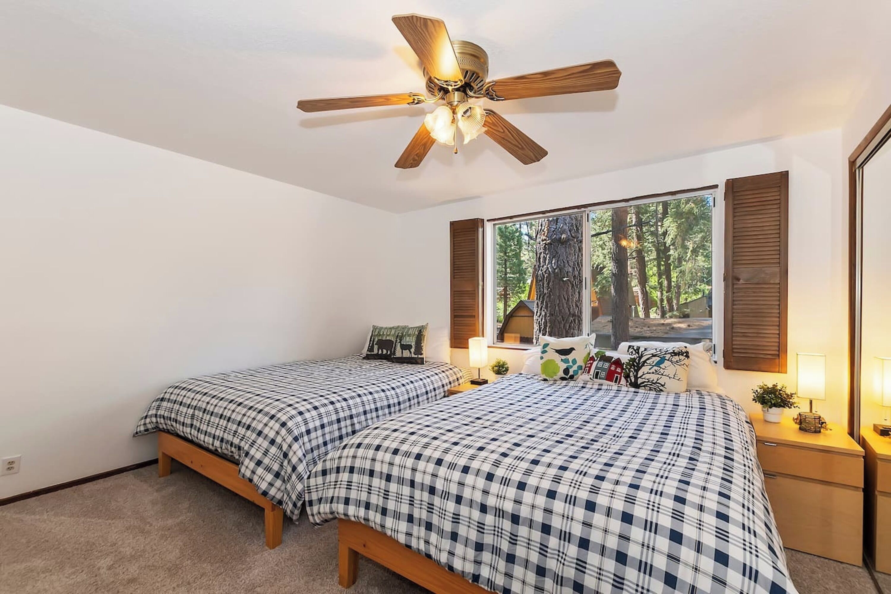 Une chambre avec deux lits, un ventilateur de plafond, une grande fenêtre donnant sur la forêt et des tables de chevet avec des lampes.