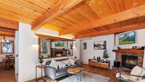 A spacious living room with a fireplace, wooden ceiling beams, and a cozy seating area. - Summit Happy Mountain Cabin (Big Bear Lake)