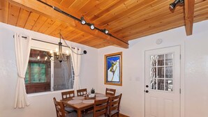 A dining area with a wooden table and chairs, a chandelier, and a window with curtains. - Summit Happy Mountain Cabin (Big Bear Lake)