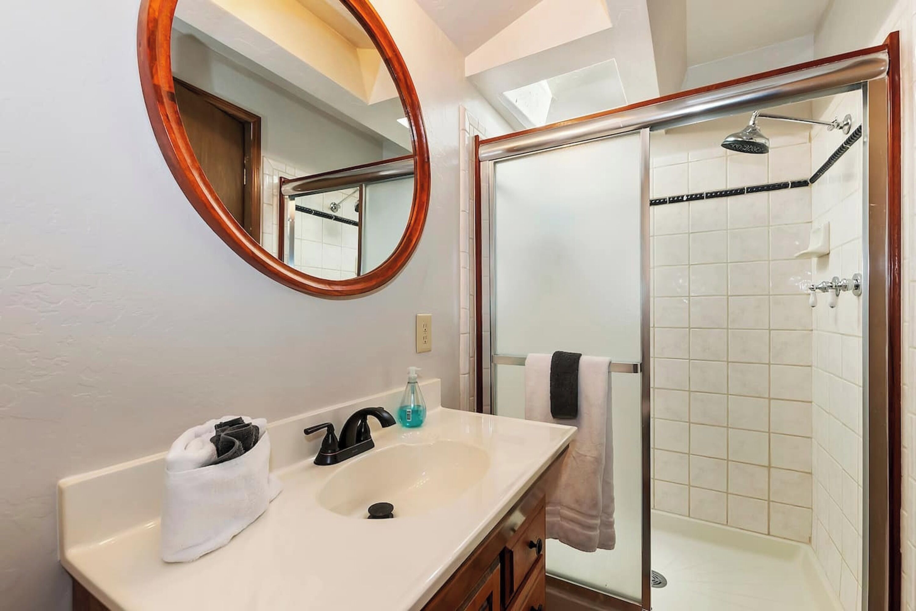 A bathroom with a white sink, a mirror with a wooden frame, a glass shower enclosure, and a towel rack.