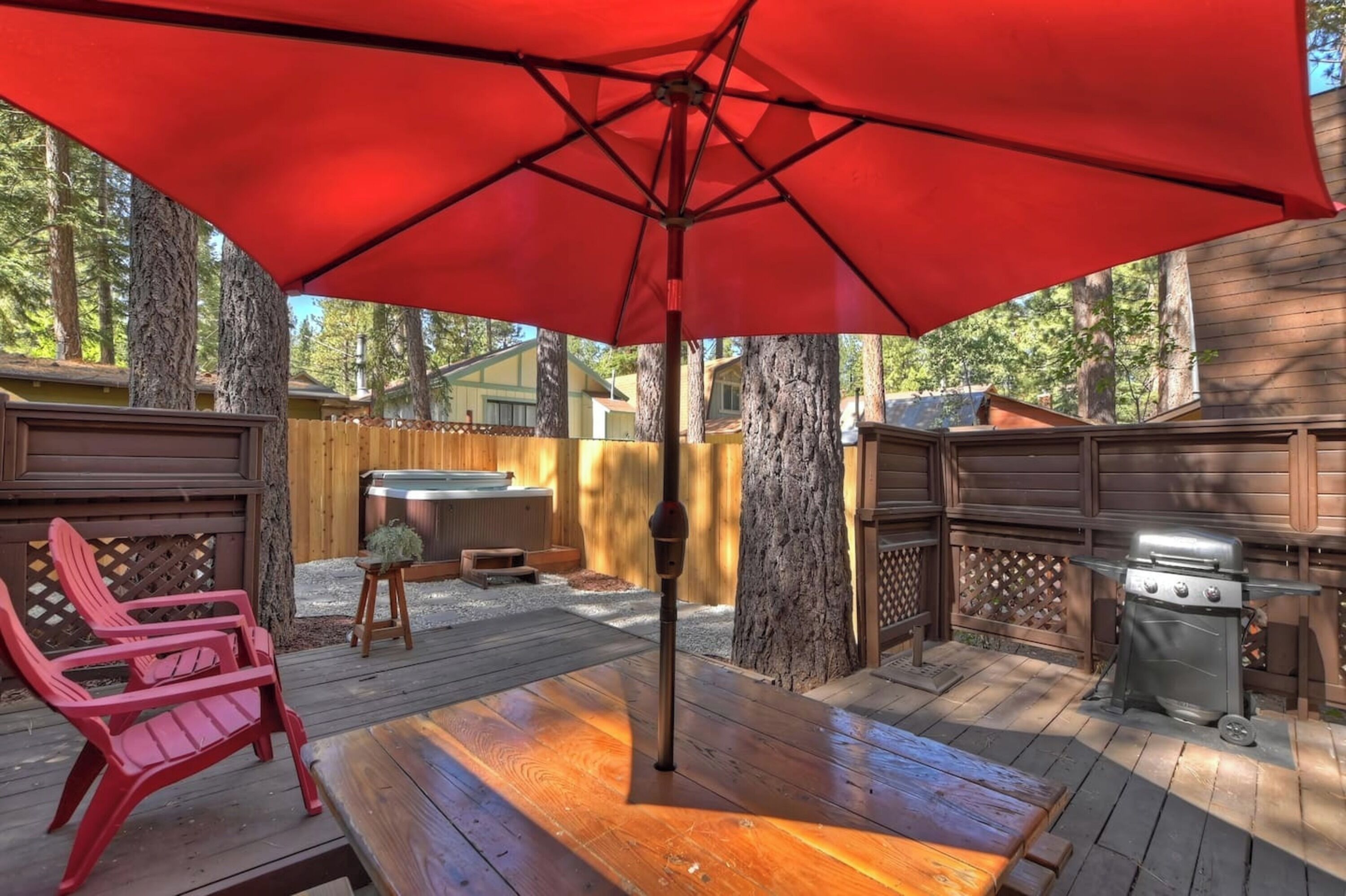 Une terrasse extérieure avec une plateforme en bois, des chaises rouges, un barbecue et un parasol rouge.